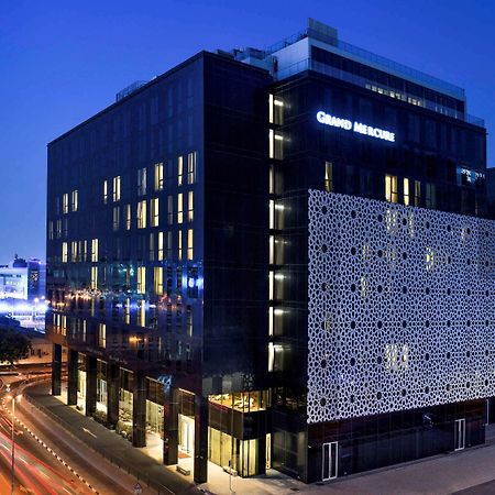 Grand Mercure Dubai City Εξωτερικό φωτογραφία The photo shows a modern building at night, featuring a sleek, contemporary design. The building has a large facade with a distinctive patterned wall on one side. Illuminated signs display the name "Grand Maison." Surrounding the building, there are 
