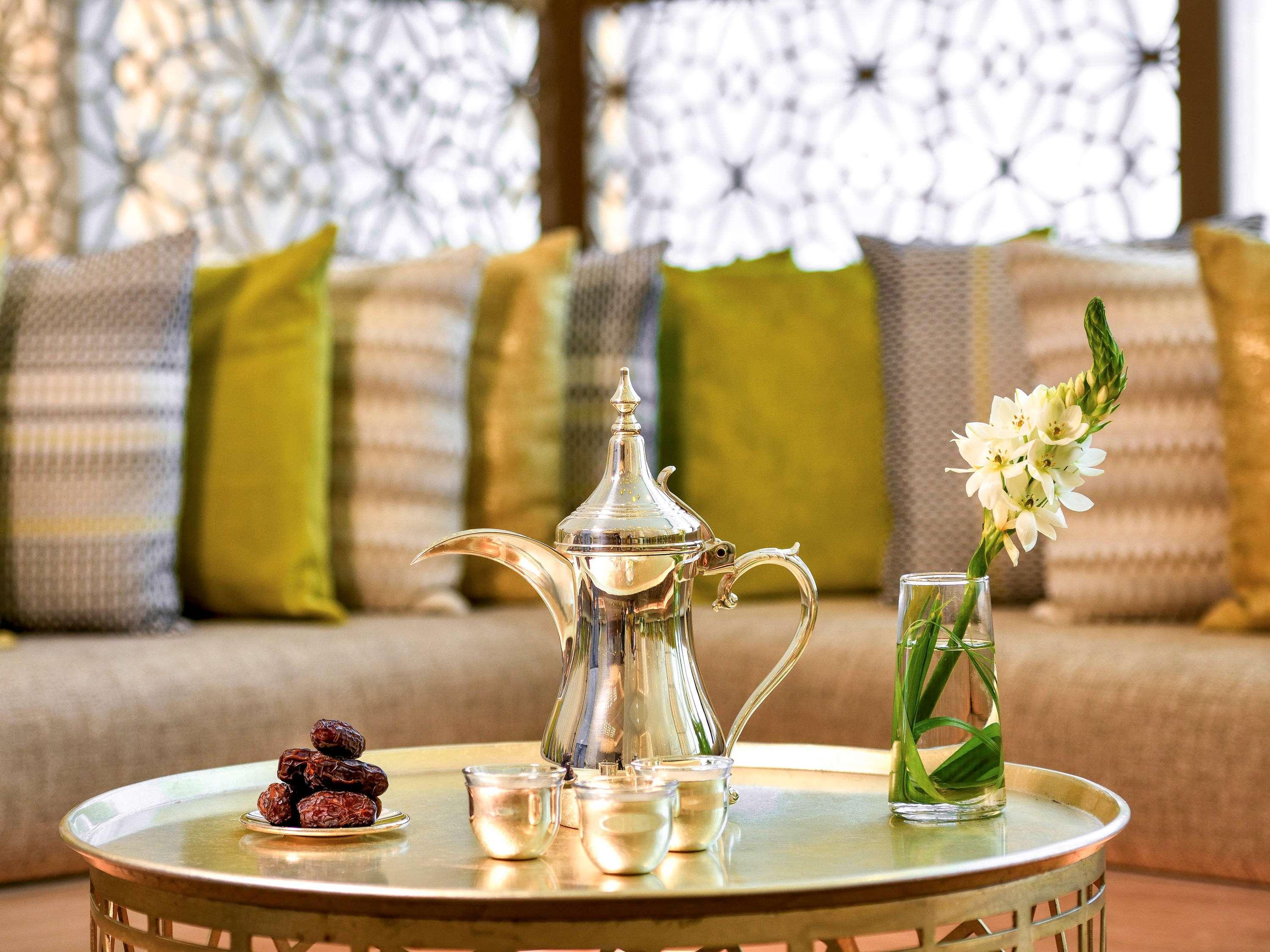Grand Mercure Dubai City Εξωτερικό φωτογραφία The photo features a decorative table with a shiny silver coffee pot and a small set of cups, indicating a traditional beverage service. Around the pot, there are some dates placed on a small dish. In addition, a clear glass vase holds a few green st