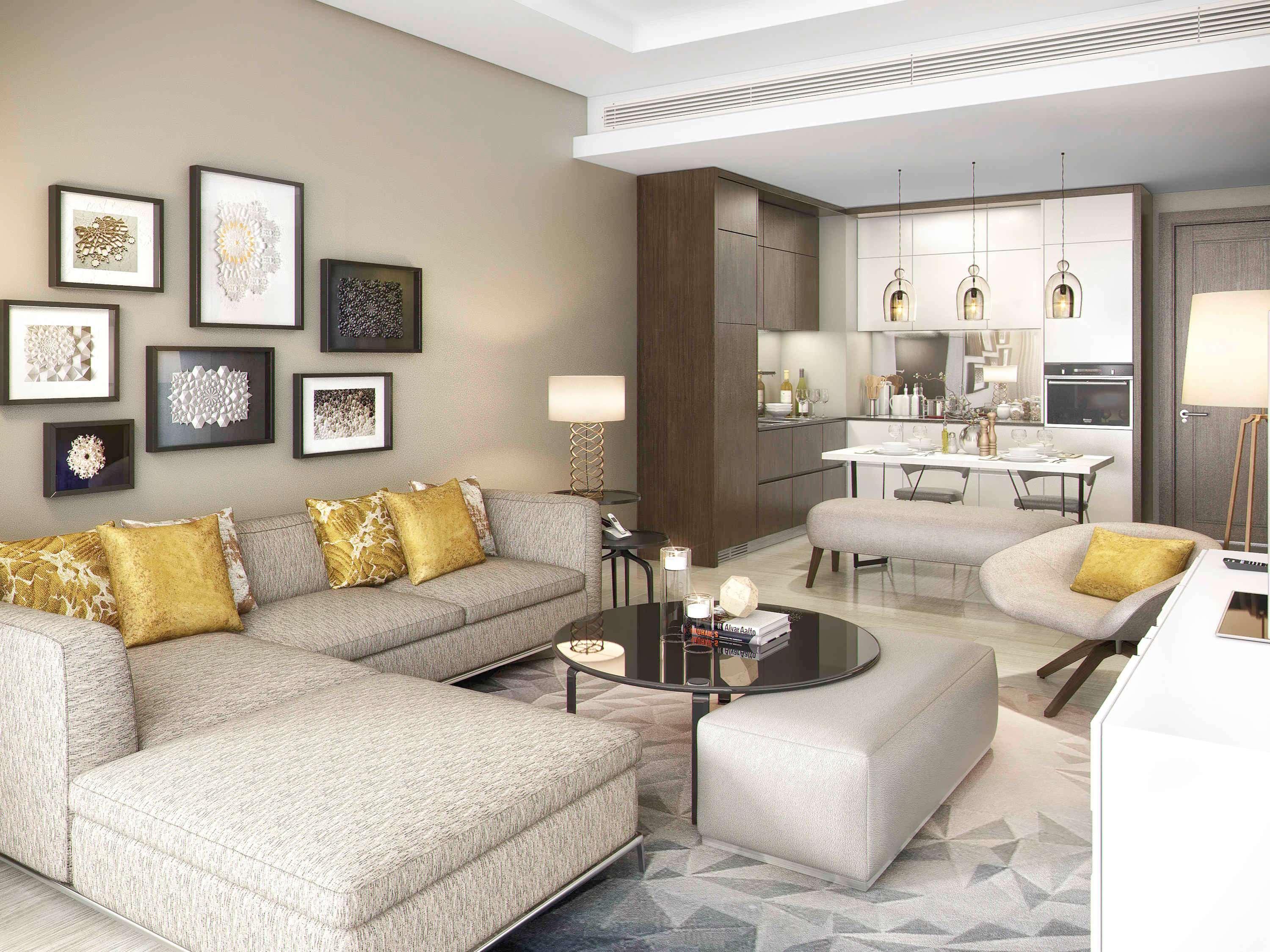 Grand Mercure Dubai City Εξωτερικό φωτογραφία The photo shows a modern living room and kitchen area. The living room features a light-colored sectional sofa with decorative pillows in shades of gold. There is a round black coffee table placed in front of the sofa. On the wall, there are several 