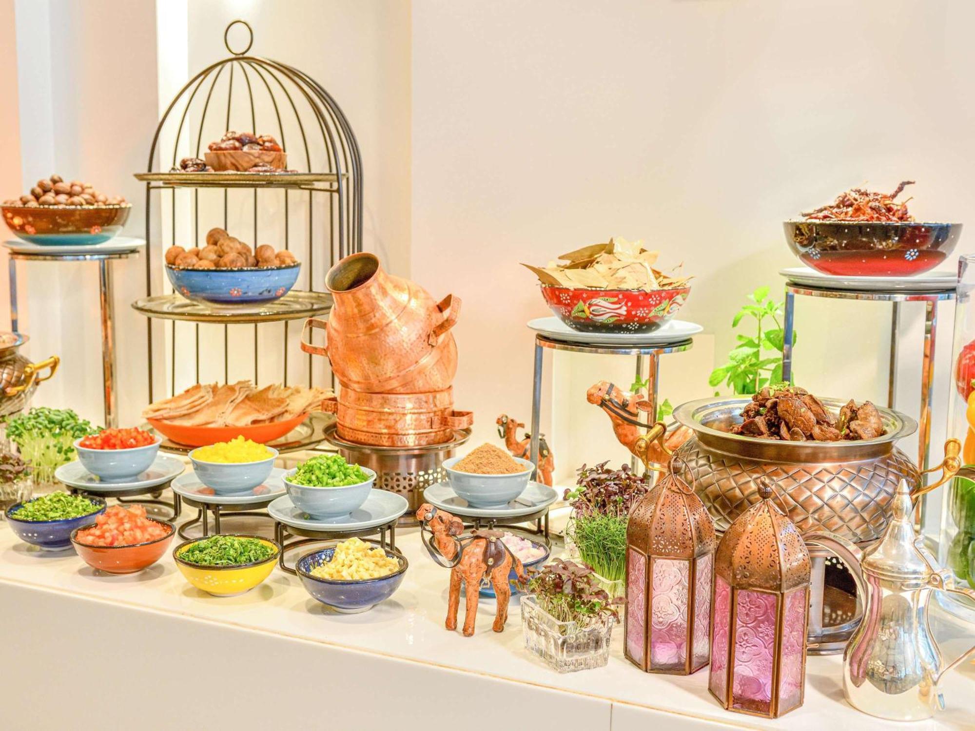 Grand Mercure Dubai City Εξωτερικό φωτογραφία The photo displays a vibrant and elaborate buffet setup featuring a variety of dishes. On one side, there's a decorative metal stand with several tiers holding different types of foods, likely including cooked meats and other savory items. 

In the f
